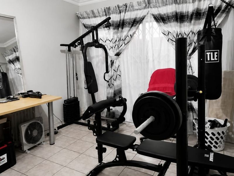 A functional home gym space featuring tiled flooring and a security gate, currently utilized for fitness equipment and storage.