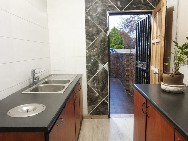 A functional scullery area featuring double sinks, dark laminate countertops, built-in cabinetry, and direct access to an exterior courtyard through a security gate.