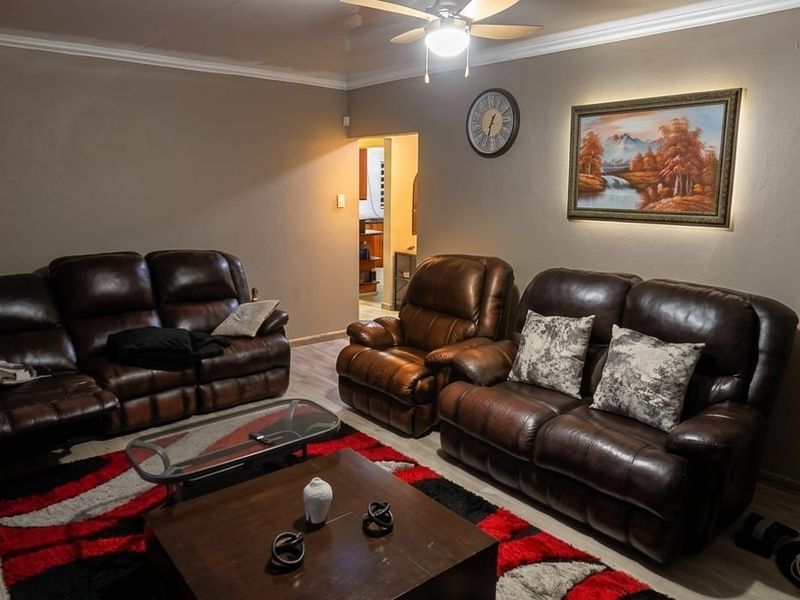 A comfortable living room featuring laminate flooring, a ceiling fan, and decorative cove cornicing, providing a functional space for relaxation.