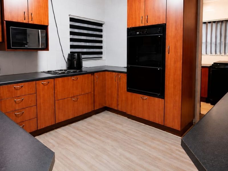 A functional kitchen featuring wood-look cabinetry, dark laminate countertops, built-in oven, and electric hob with a tiled backsplash.