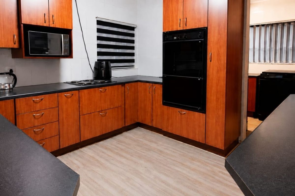 A functional kitchen featuring wood-look cabinetry, dark laminate countertops, built-in oven, and electric hob with a tiled backsplash.