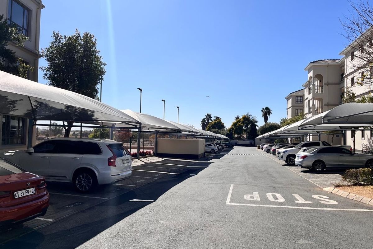 Outdoor parking area featuring covered shade-cloth carports situated between apartment building blocks.