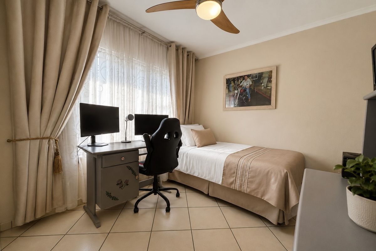 A functional bedroom featuring tiled flooring and a ceiling fan, currently utilized as a combined sleeping and workspace area.