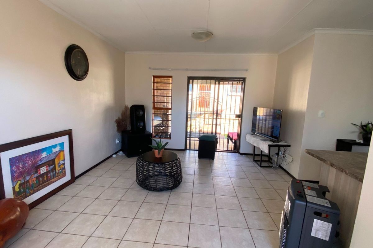 A living room featuring ceramic floor tiles, a sliding glass door with security gate, and a breakfast bar connecting to the kitchen area.
