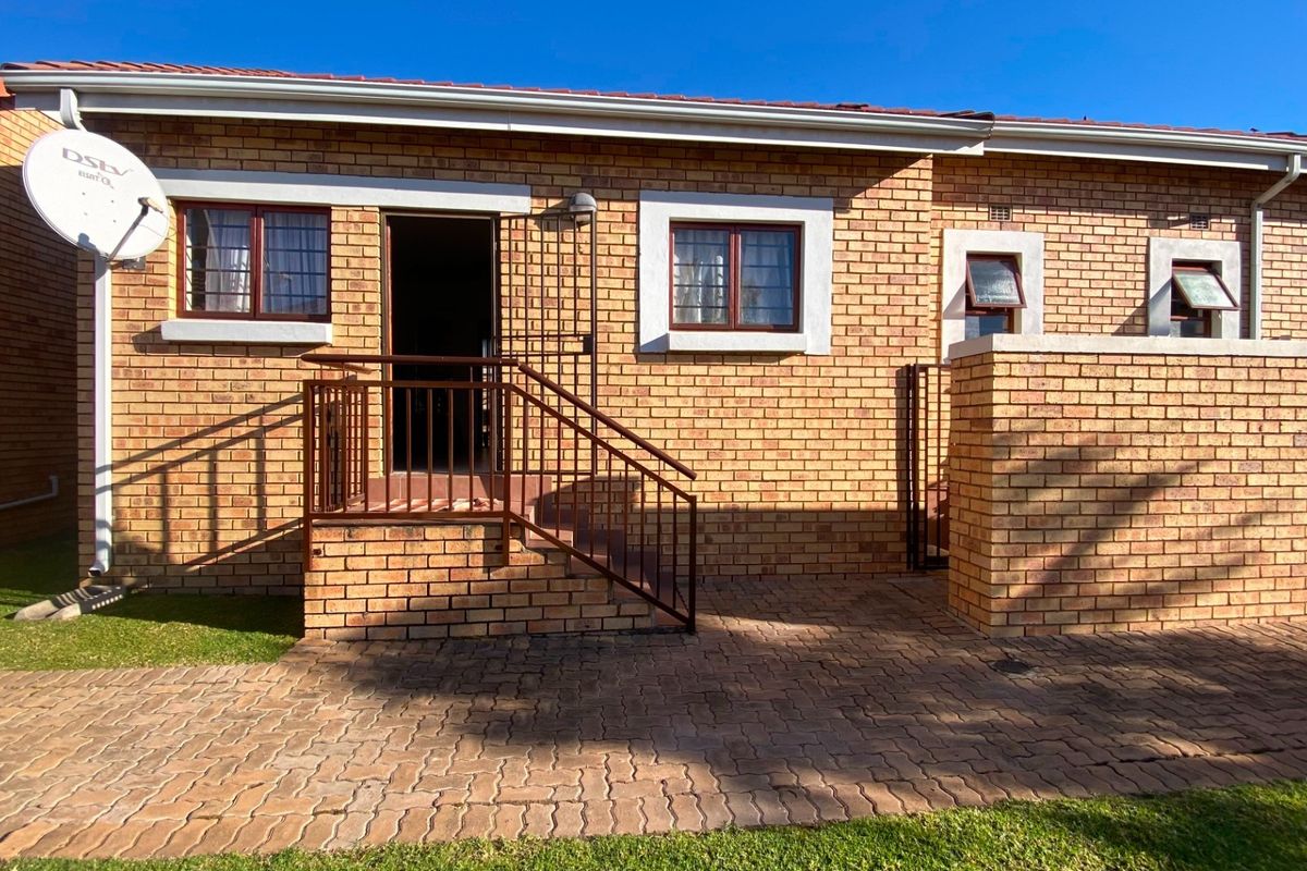 Rear exterior view of the townhouse featuring a face brick facade, paved patio area, and secure metal railing at the entrance.