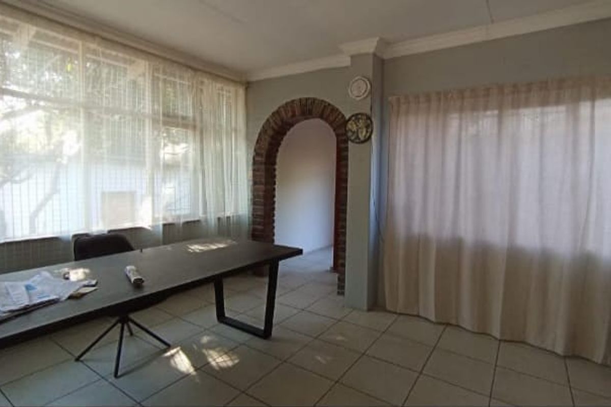A living area featuring tiled flooring, large windows with curtains, and a distinctive brick archway leading to an adjacent space.