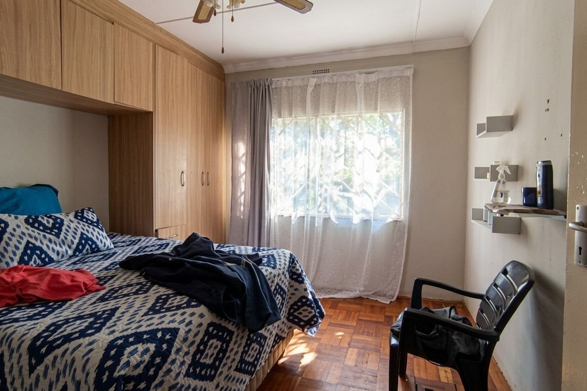 A bedroom featuring built-in wooden cabinetry, parquet flooring, and a ceiling fan, offering functional storage and natural light.