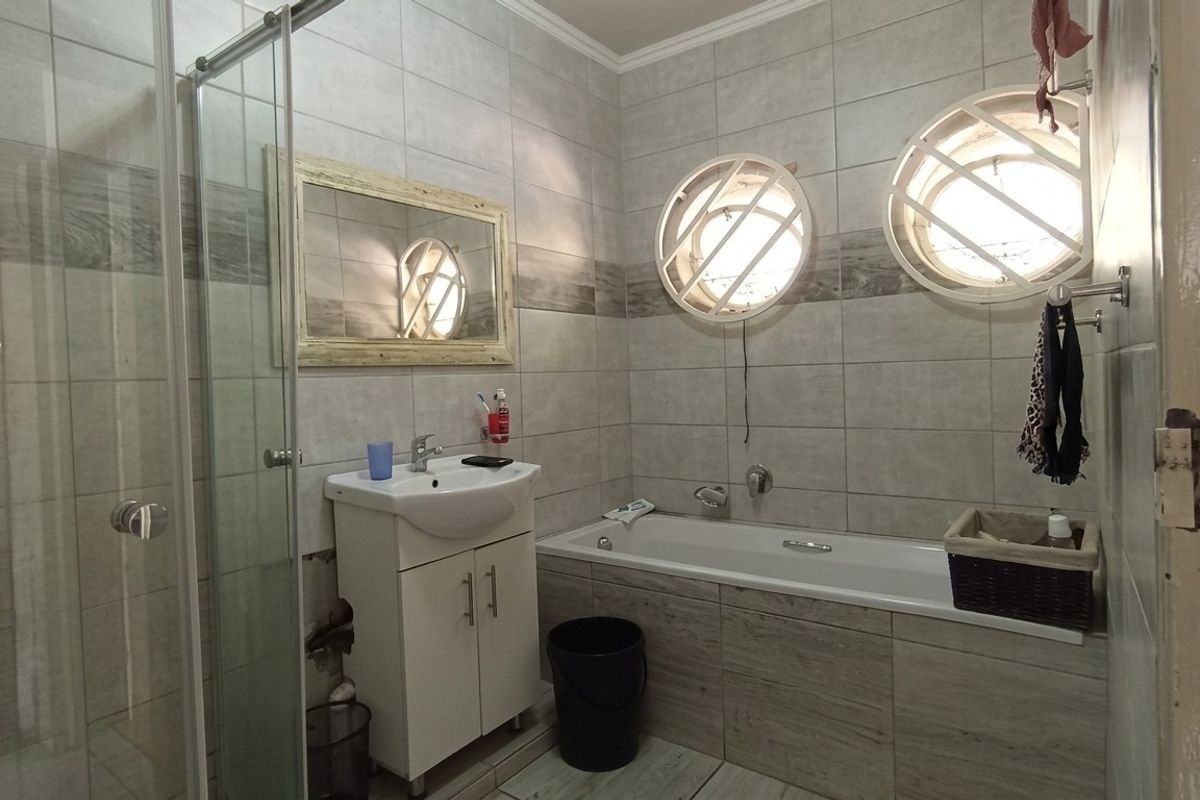 A bathroom featuring a glass-enclosed shower, a built-in bathtub, a vanity basin, and distinctive circular windows with tiled walls.