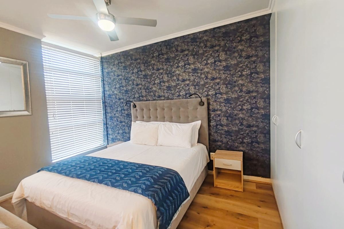A well-maintained bedroom featuring wood-look flooring, a decorative accent wall, built-in cupboards, and a ceiling fan.