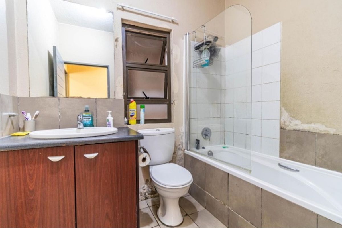A functional bathroom featuring a vanity cabinet, toilet, and a shower-over-bath combination with a glass screen.