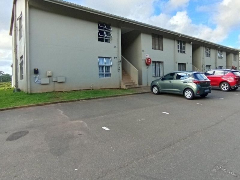 Exterior view of a multi-story apartment complex featuring paved parking area and communal stairwell access.