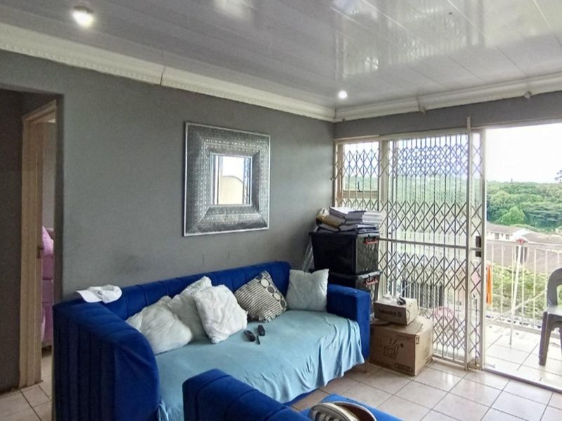 A living room featuring tiled flooring, recessed ceiling lighting, and a sliding door leading to a balcony with security gate.