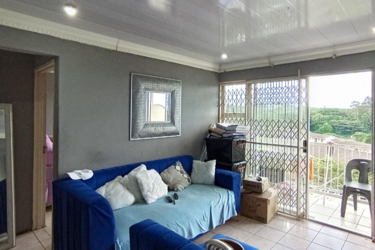 A living room featuring tiled flooring, recessed ceiling lighting, and a sliding door leading to a balcony with security gate.