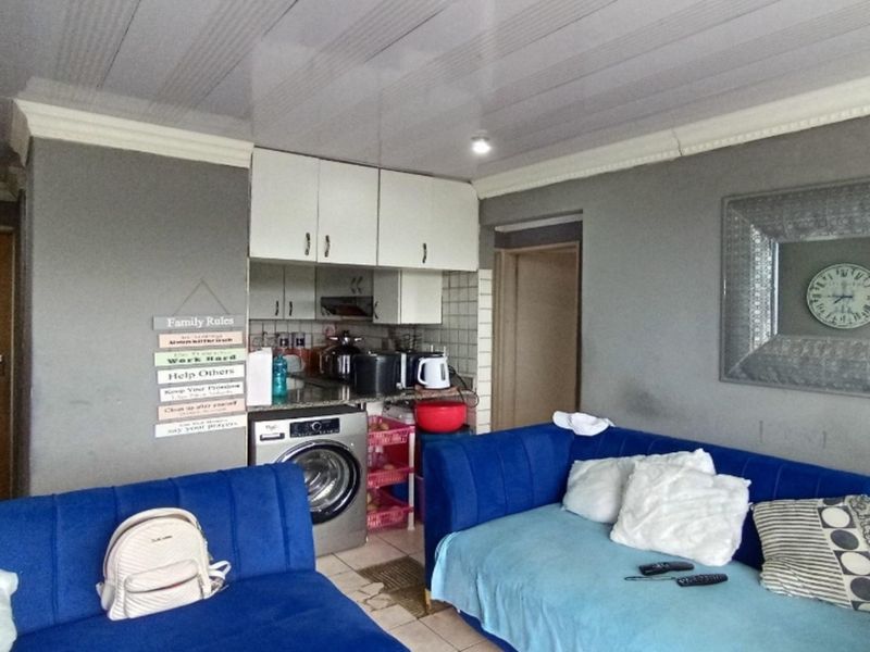 An open-plan living area featuring a compact kitchen corner with built-in cabinetry and an integrated laundry appliance.