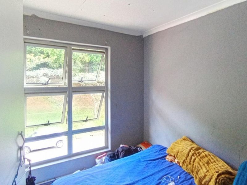 A compact bedroom featuring grey painted walls, a large aluminium-framed window, and coved ceiling detailing.