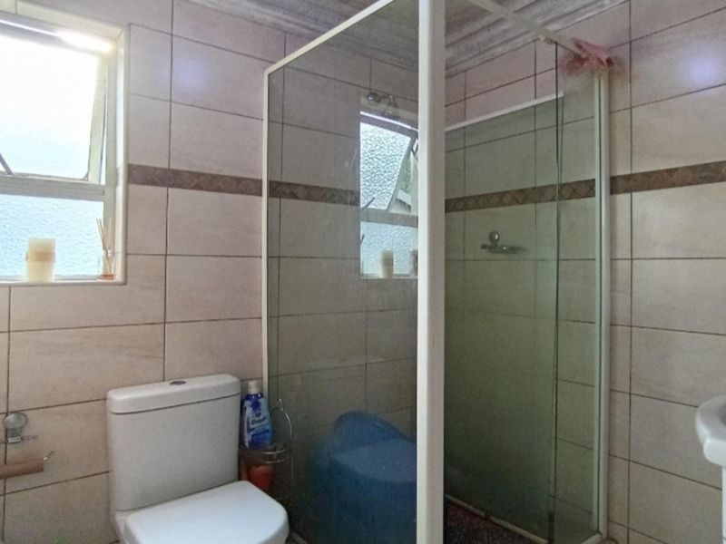 A functional bathroom featuring a glass-enclosed shower, ceramic wall tiling, a standard toilet, and a pedestal basin.