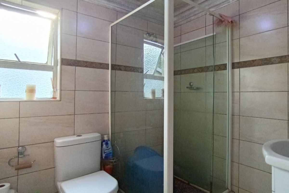 A functional bathroom featuring a glass-enclosed shower, ceramic wall tiling, a standard toilet, and a pedestal basin.