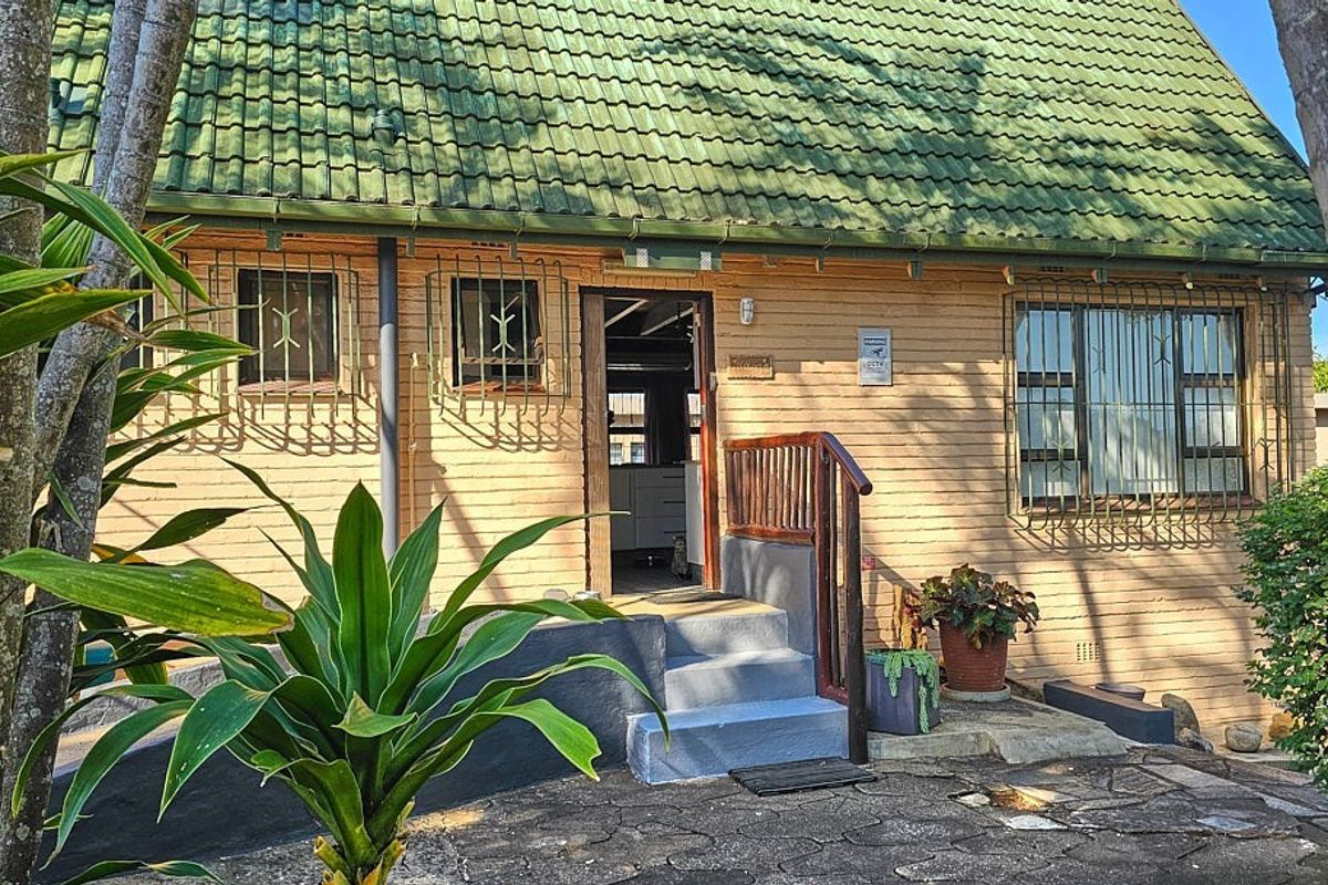Exterior view of a brick house featuring a green tiled roof, security bars on windows, and concrete entrance steps.