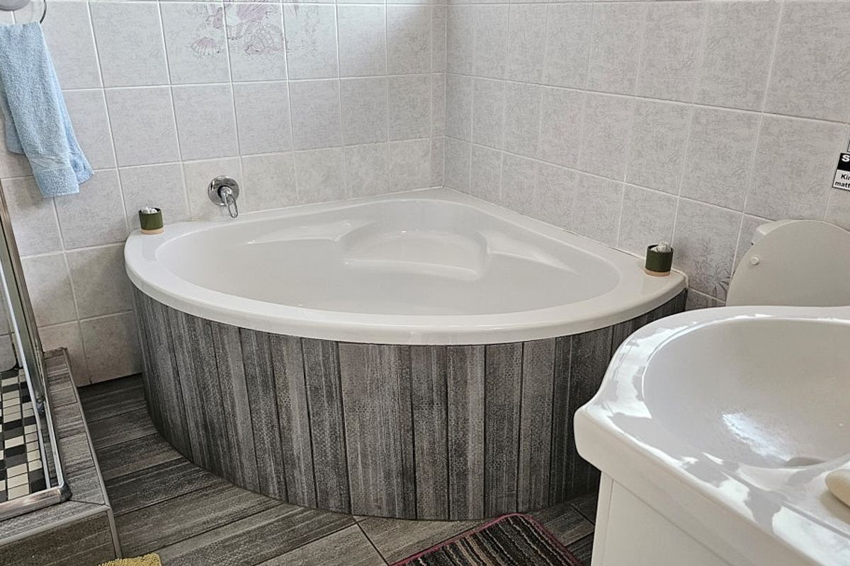 A bathroom featuring a corner bathtub with wood-look paneling, tiled walls, a shower enclosure, and a pedestal sink.