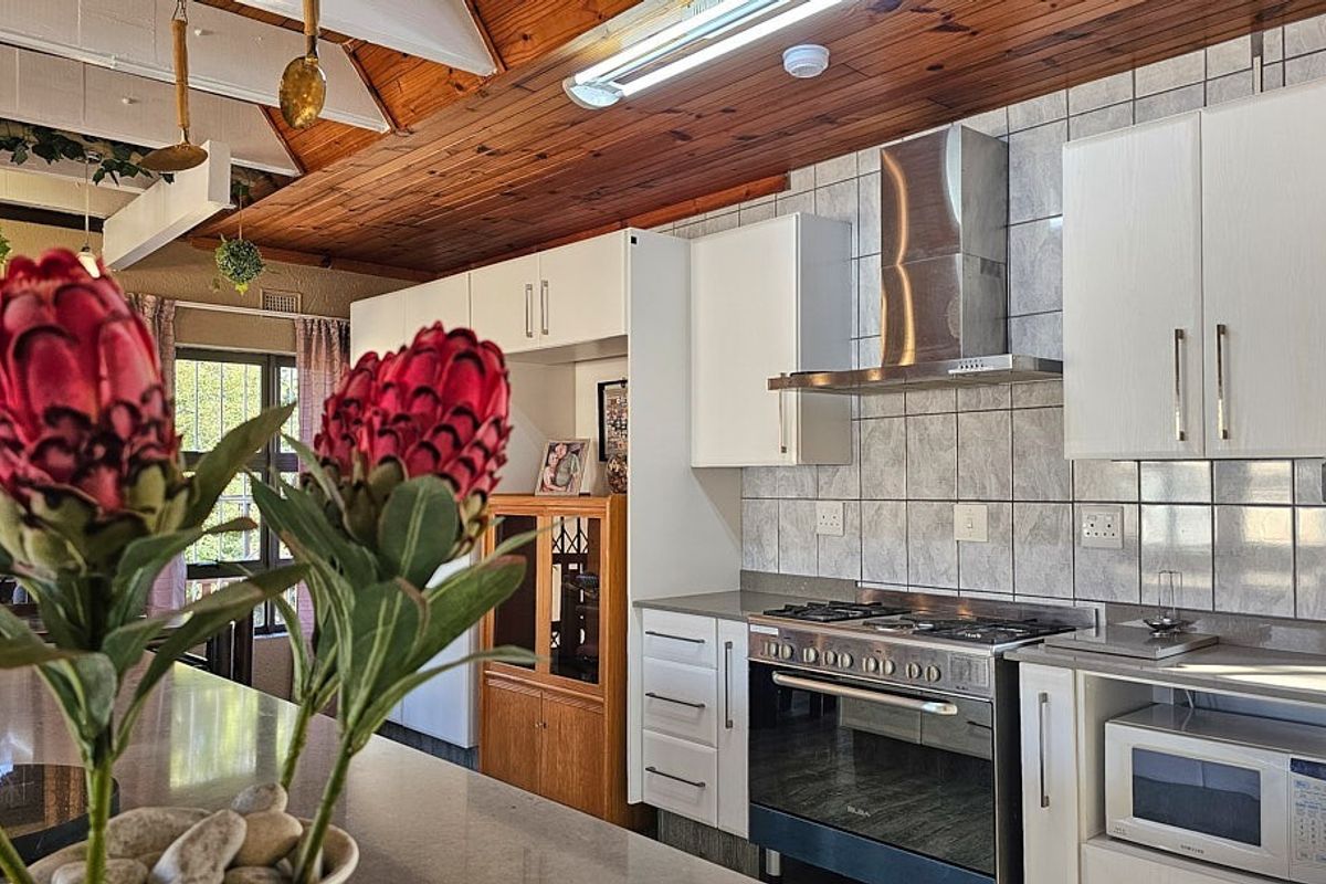 Kitchen featuring white cabinetry, stainless steel gas stove with extractor fan, and a timber-paneled ceiling with exposed beams.