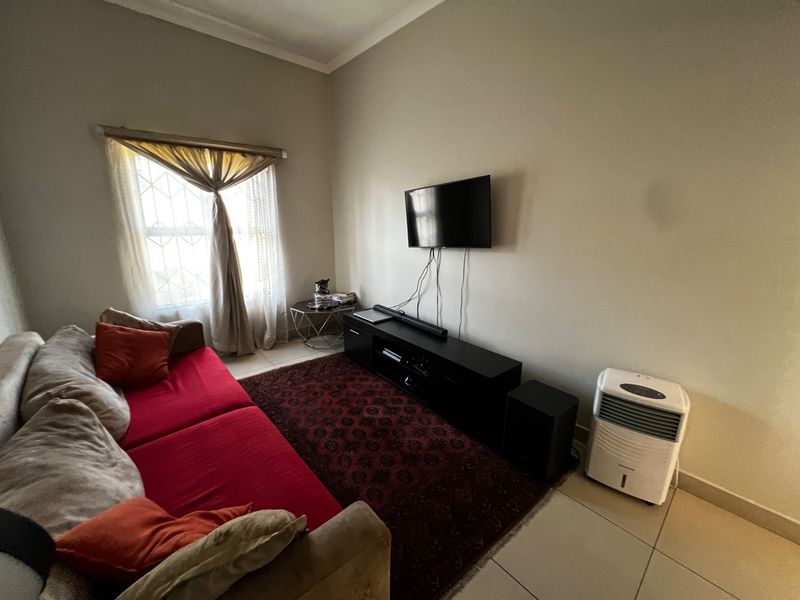 A living room featuring tiled flooring, a window with security bars, and wall-mounted television setup.