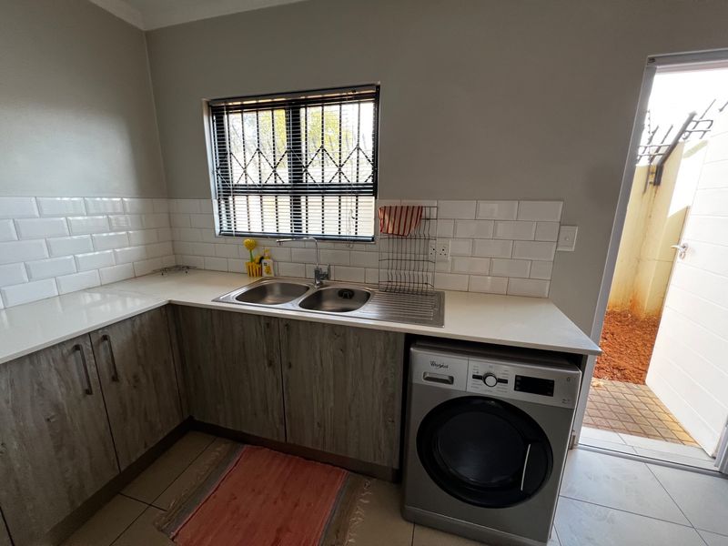 A functional kitchen featuring subway tile backsplash, double basin sink, stone-look countertops, and built-in cabinetry with space for a washing machine.