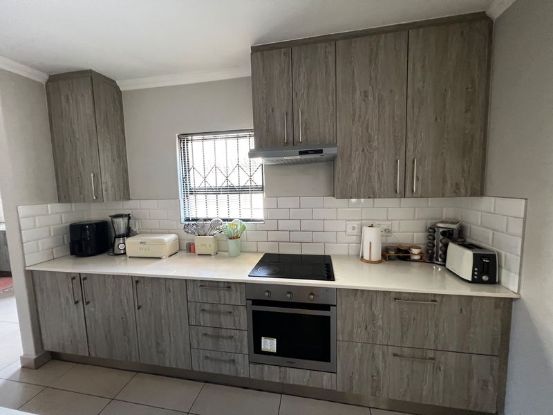Modern kitchen featuring wood-grain cabinetry, white subway tile backsplash, stone countertops, built-in electric oven, and glass cooktop with extractor fan.