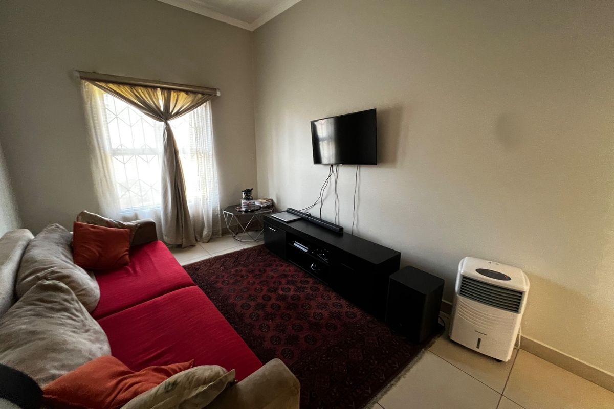 A living room featuring tiled flooring, a window with security bars, and wall-mounted television setup.