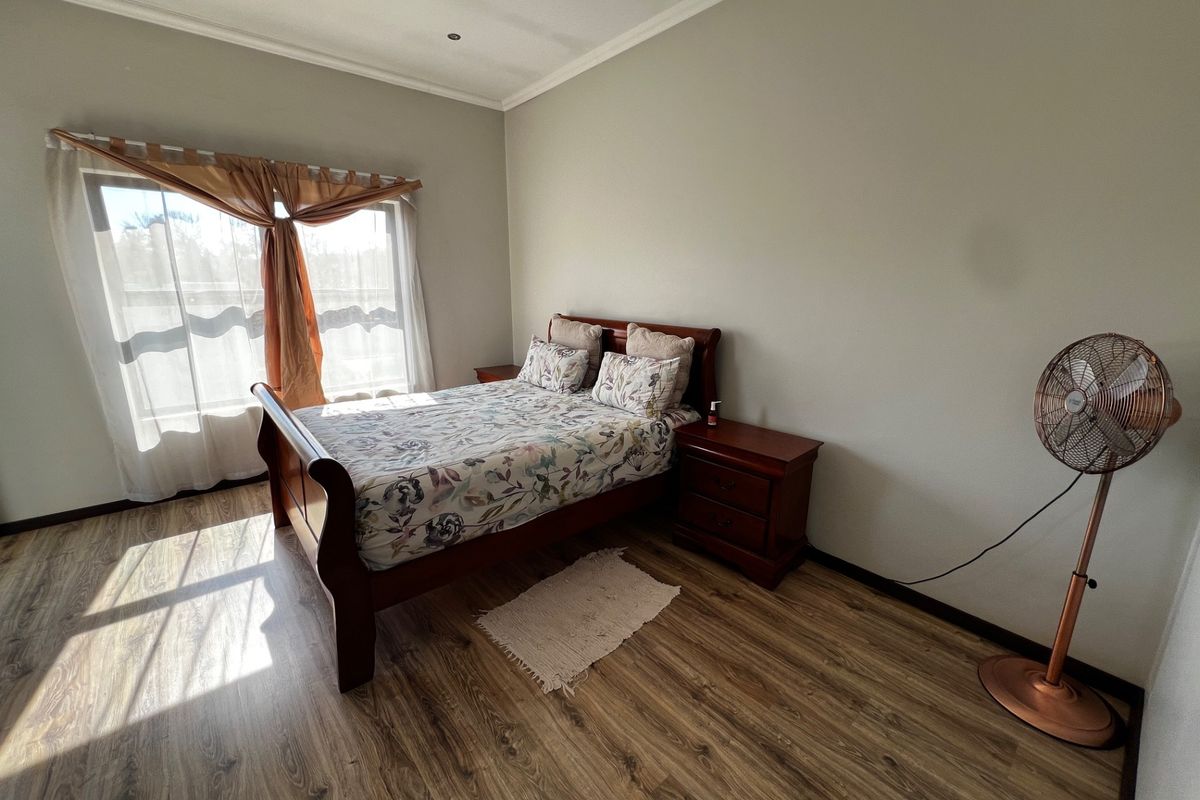 A well-lit bedroom featuring wood-look laminate flooring, neutral wall tones, and a large window with natural light.
