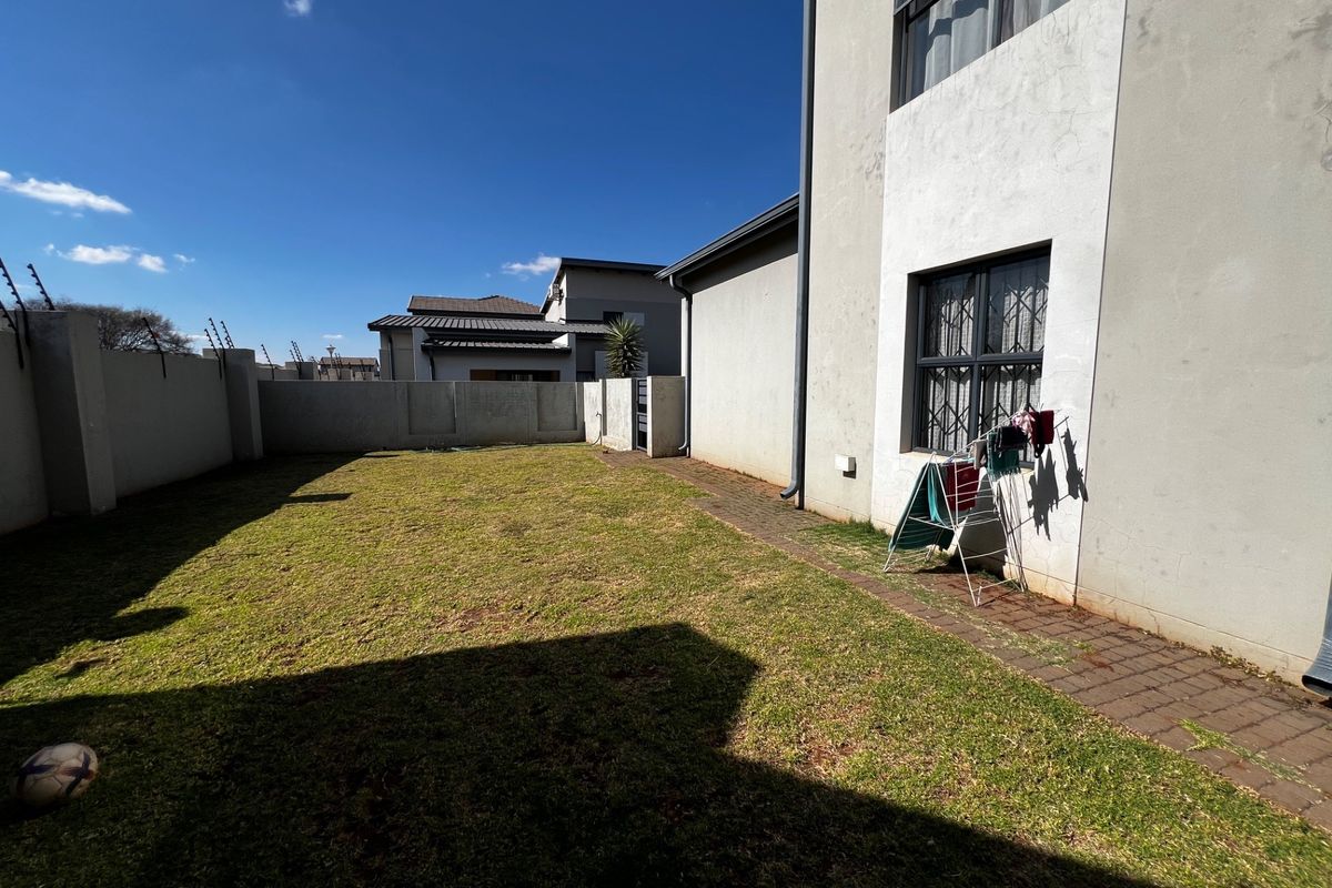 A private rear garden featuring a paved walkway, perimeter boundary walls with electric fencing, and a grassed lawn area.