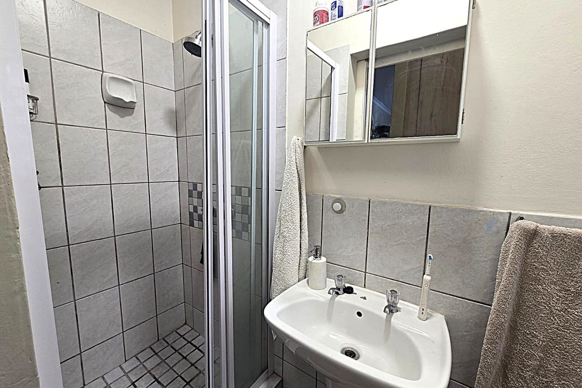 A functional bathroom featuring a shower enclosure, pedestal basin, and a mirrored medicine cabinet with tiled wall finishes.
