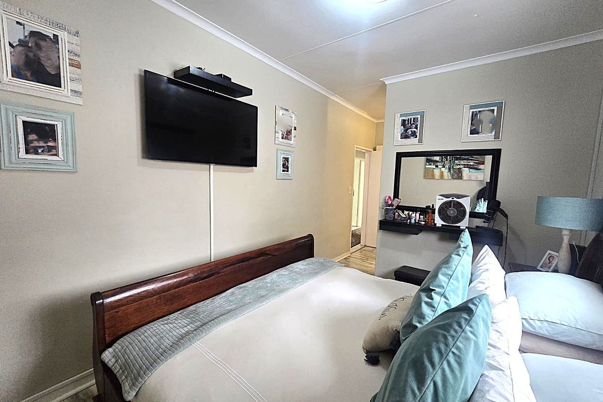 A well-maintained bedroom featuring neutral wall tones, cove cornicing, and a wall-mounted television setup.