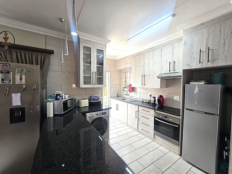 A functional kitchen featuring granite countertops, built-in cabinetry, integrated oven and hob, and tiled flooring with ample workspace.