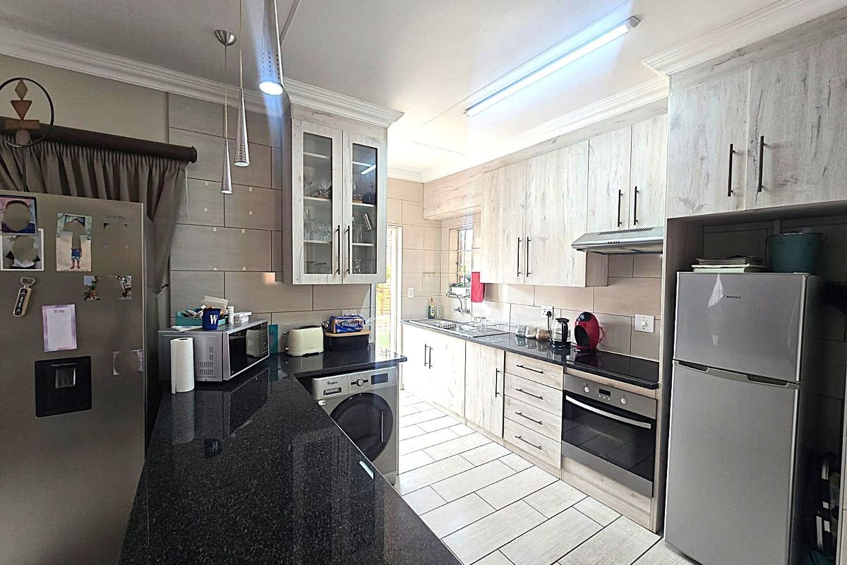 A functional kitchen featuring granite countertops, built-in cabinetry, integrated oven and hob, and tiled flooring with ample workspace.