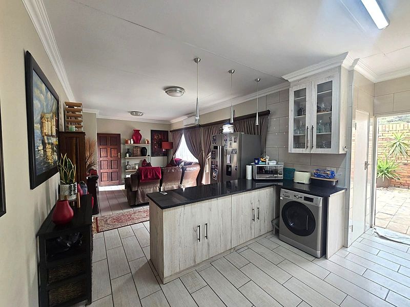 Open-plan living and kitchen area featuring tiled flooring, granite countertops, integrated laundry appliance, and glass-fronted cabinetry with modern pendant lighting.