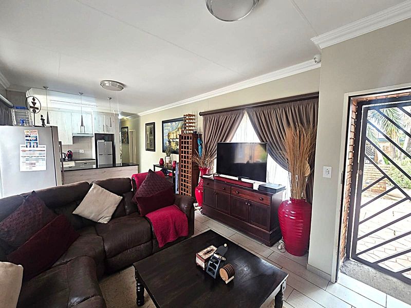 Open-plan living area featuring tiled flooring, coving, and an integrated kitchen space with cabinetry and an extractor fan, leading to a secure entrance.