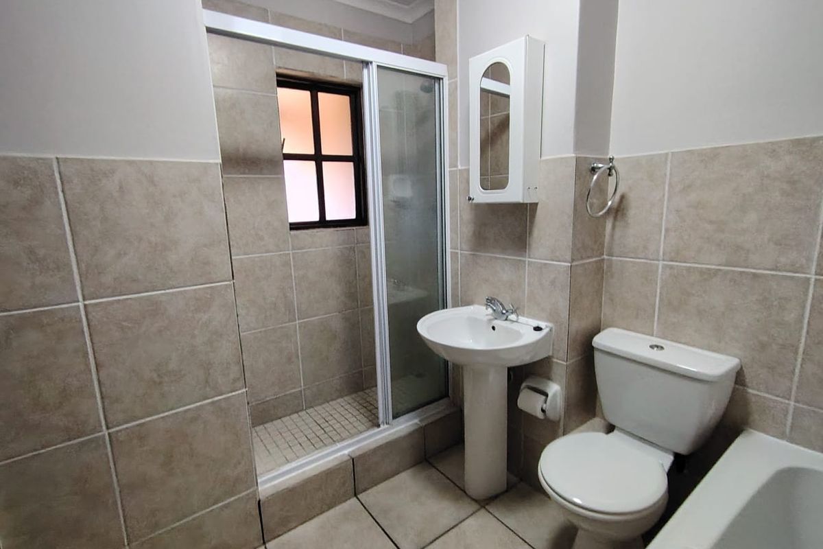 A functional bathroom featuring a walk-in shower with glass enclosure, pedestal basin, and toilet, finished with neutral wall and floor tiling.
