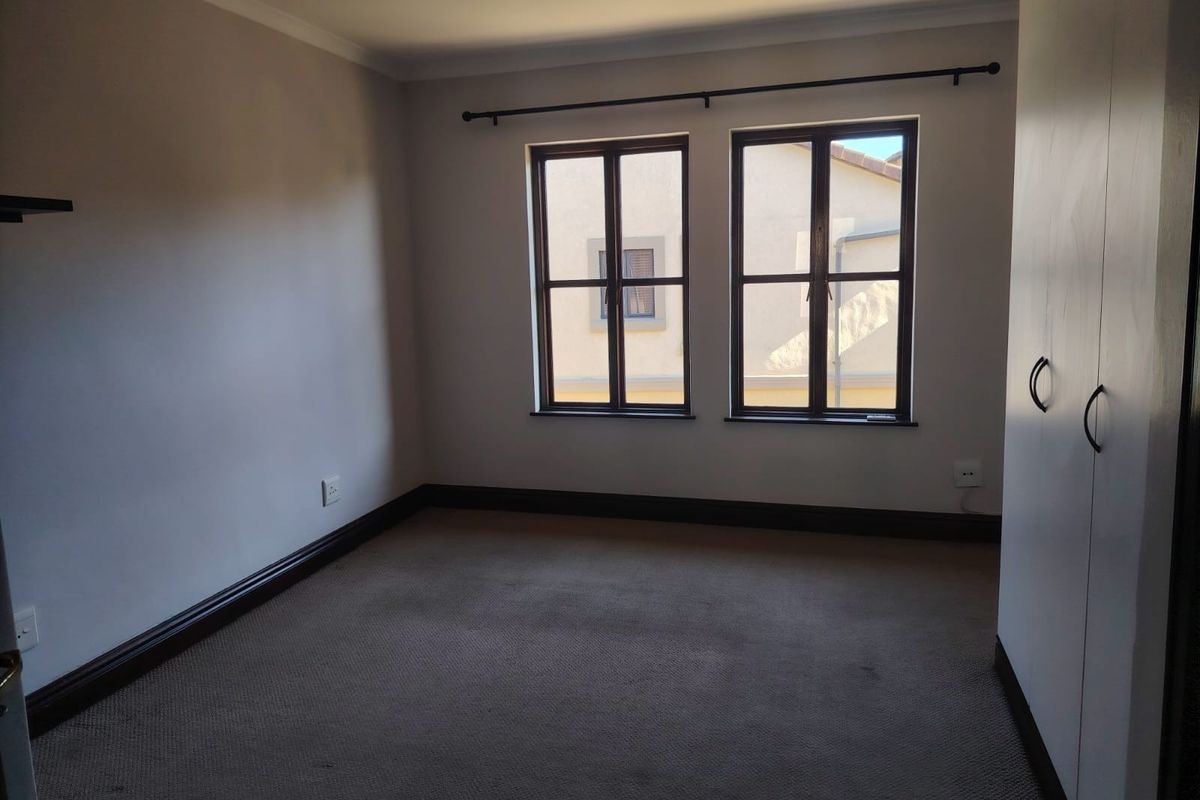 A vacant bedroom featuring neutral walls, carpeted flooring, built-in cupboards, and dark-framed windows providing natural light.