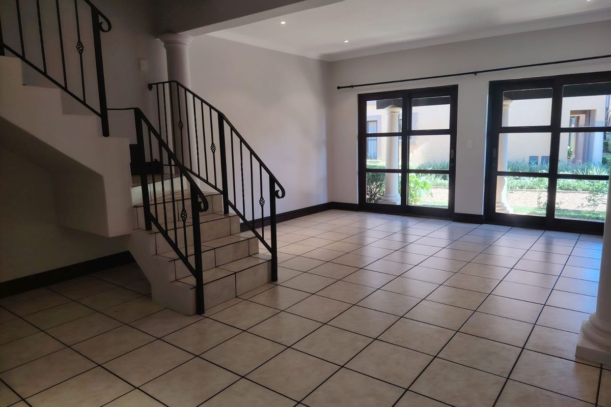 Spacious open-plan living area featuring tiled flooring, a built-in staircase with wrought iron railings, and large glass doors leading to the exterior.