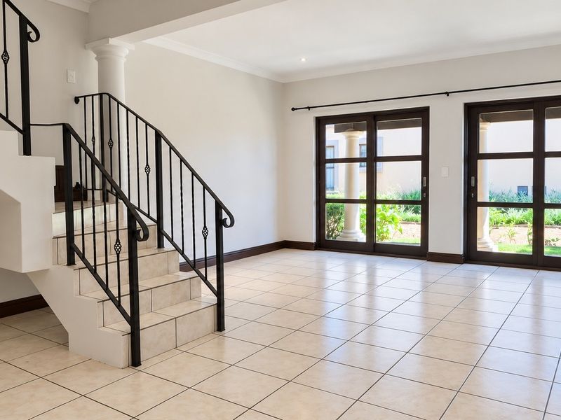 Spacious open-plan living area featuring neutral ceramic floor tiles, a classic staircase with wrought iron railing, and large sliding doors leading to the garden.