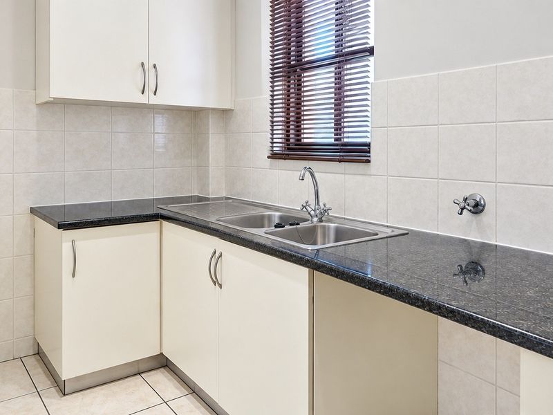 A clean, functional kitchen featuring granite countertops, stainless steel double sink, tiled splashback, and ample built-in cabinetry.