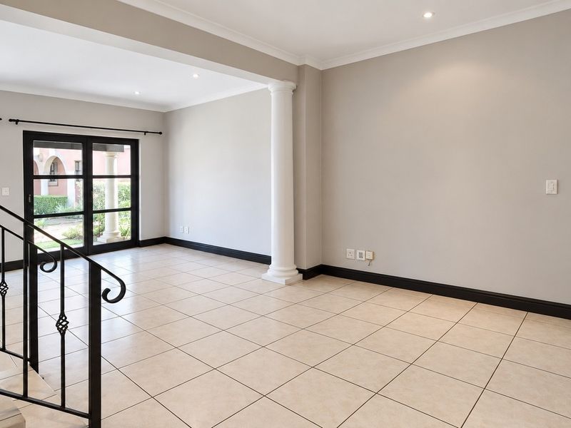 Spacious, light-filled living area featuring neutral tiled flooring, a decorative column, and direct access to the exterior through double glass doors.