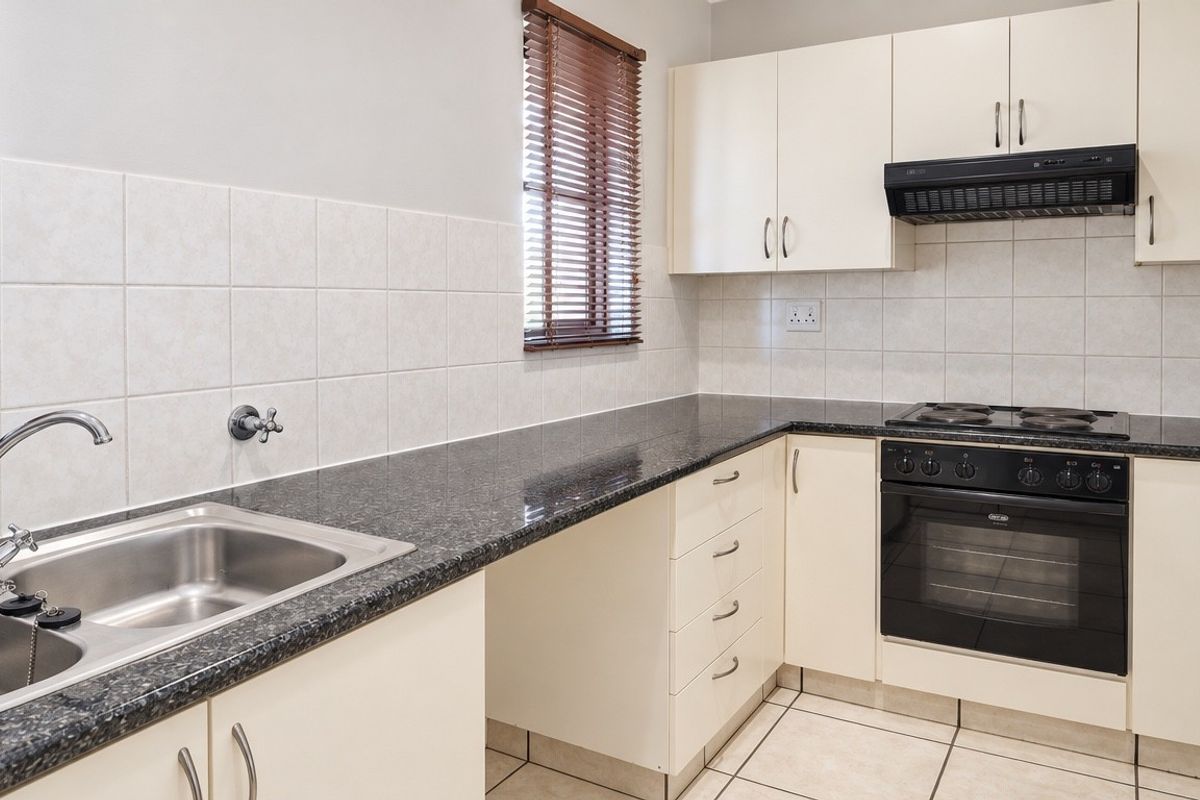 A clean and functional kitchen featuring granite countertops, built-in cabinetry, a stainless steel double sink, and integrated electric cooking appliances.