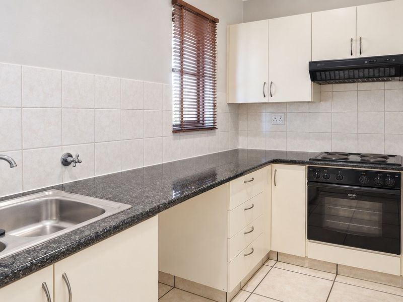 A clean and functional kitchen featuring granite countertops, built-in cabinetry, a stainless steel double sink, and integrated electric cooking appliances.