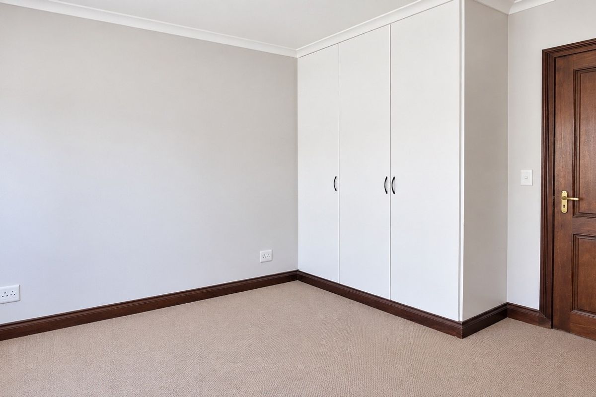 A clean, empty bedroom featuring neutral walls, carpet flooring, a built-in wardrobe, and a classic timber door.