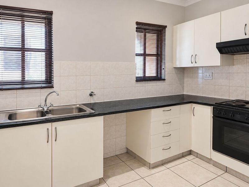 A clean, functional kitchen featuring white cabinetry, granite countertops, tiled backsplash, and integrated electric oven and hob with extractor fan.