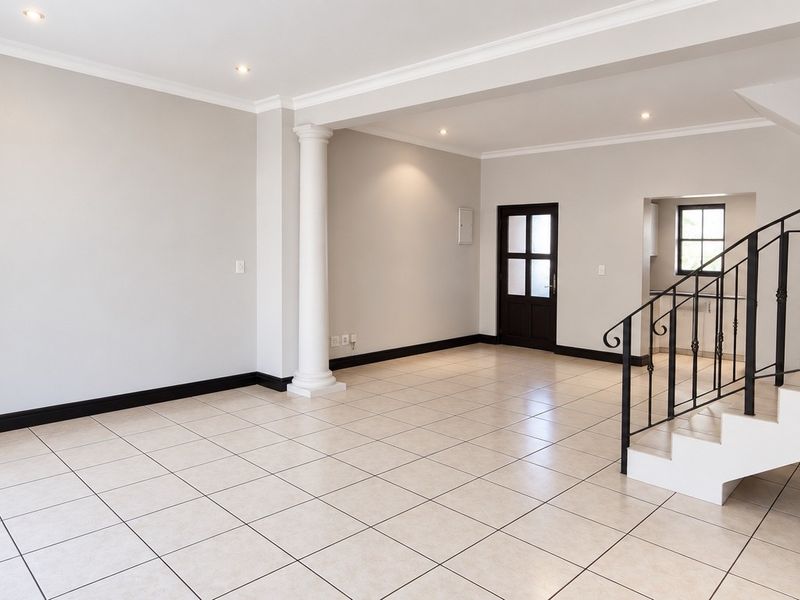 Spacious open-plan living area featuring neutral tiled flooring, a decorative column, and a staircase with a wrought iron railing.