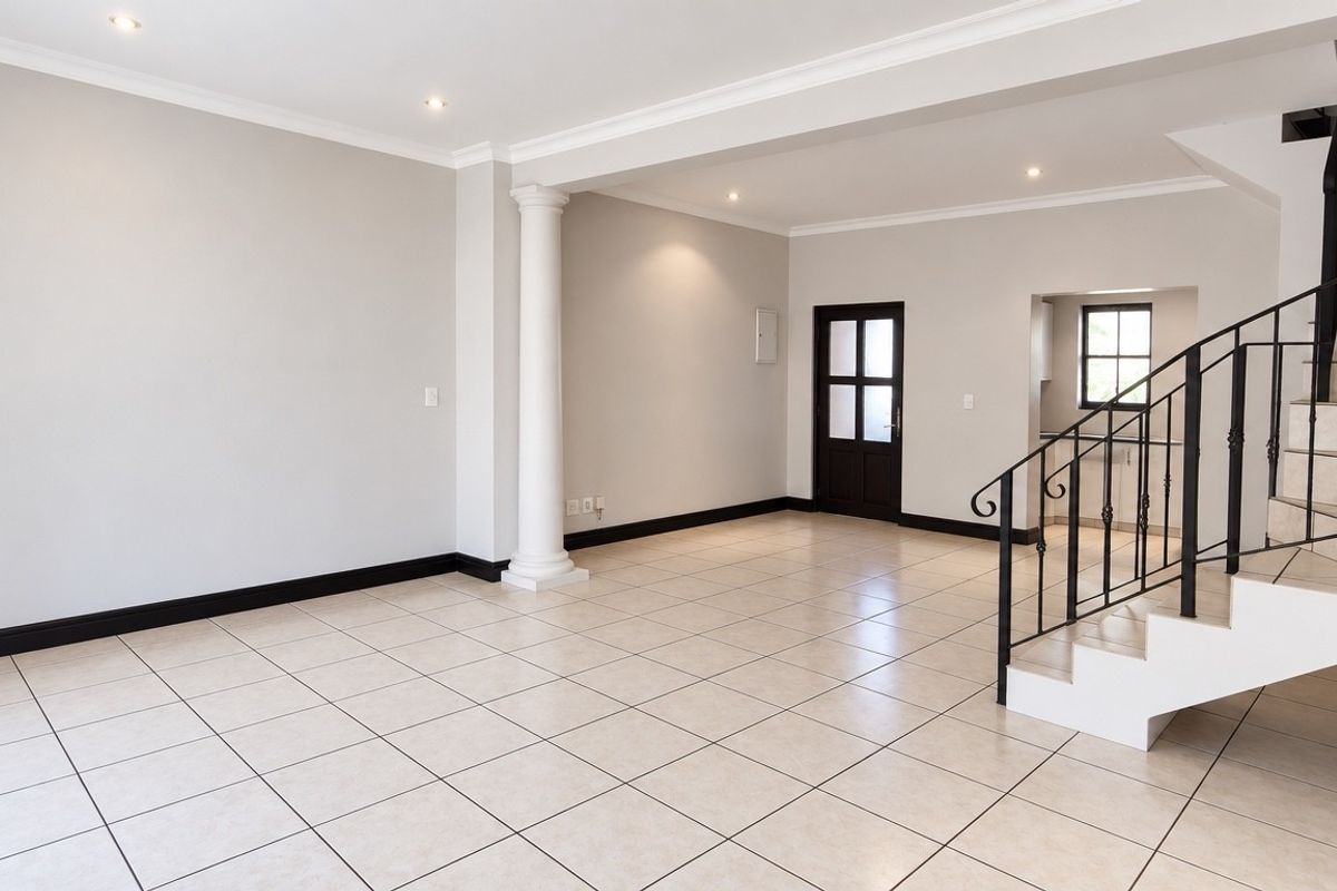 Spacious open-plan living area featuring neutral tiled flooring, a decorative column, and a staircase with a wrought iron railing.