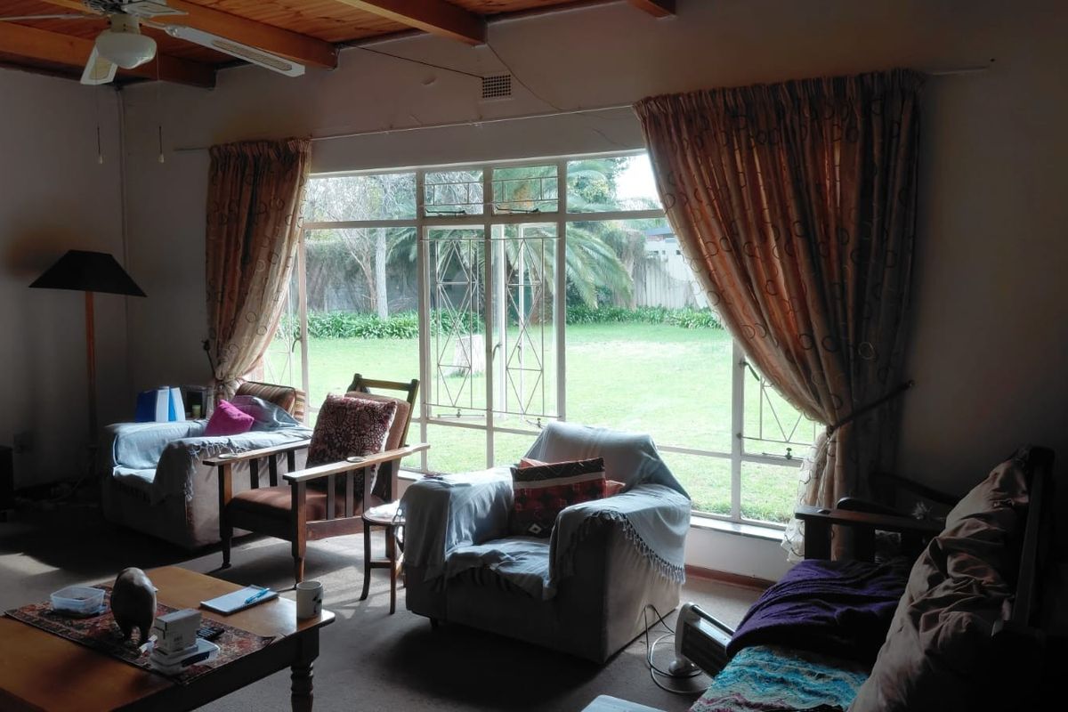 Spacious living room featuring exposed timber ceiling beams, a large window with garden views, and integrated security bars.