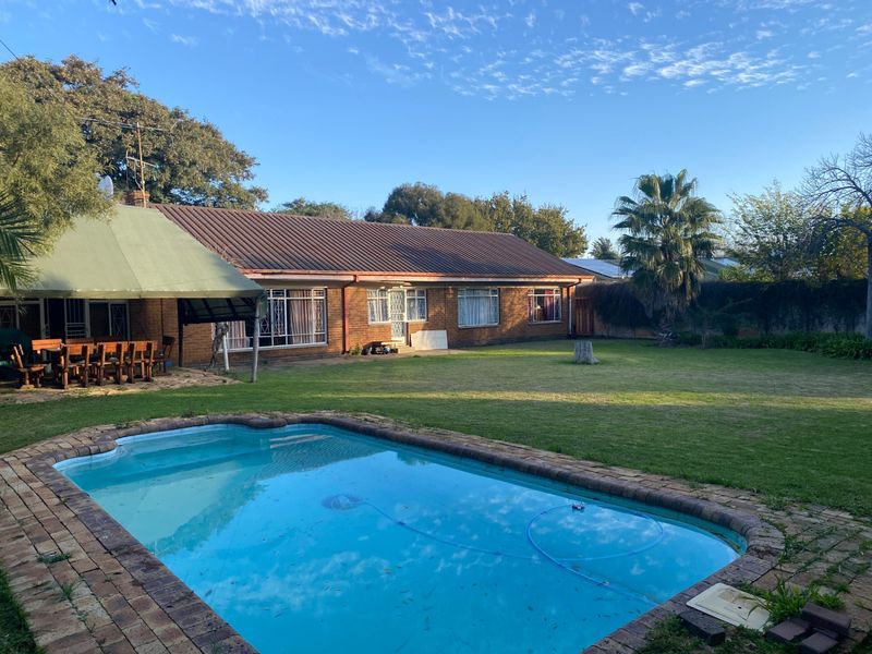 Rear view of the house featuring a swimming pool, brick-paved surround, covered patio area, and a spacious lawn.
